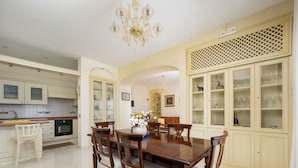 A dining room with a wooden table and chairs, a chandelier, and a kitchen in the background. - Residenza Le Sirene (Sorrento)