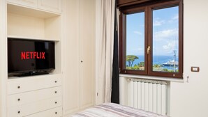 A bedroom with a television on a cabinet, a window with a view of the sea, and a radiator. - Residenza Le Sirene (Sorrento)