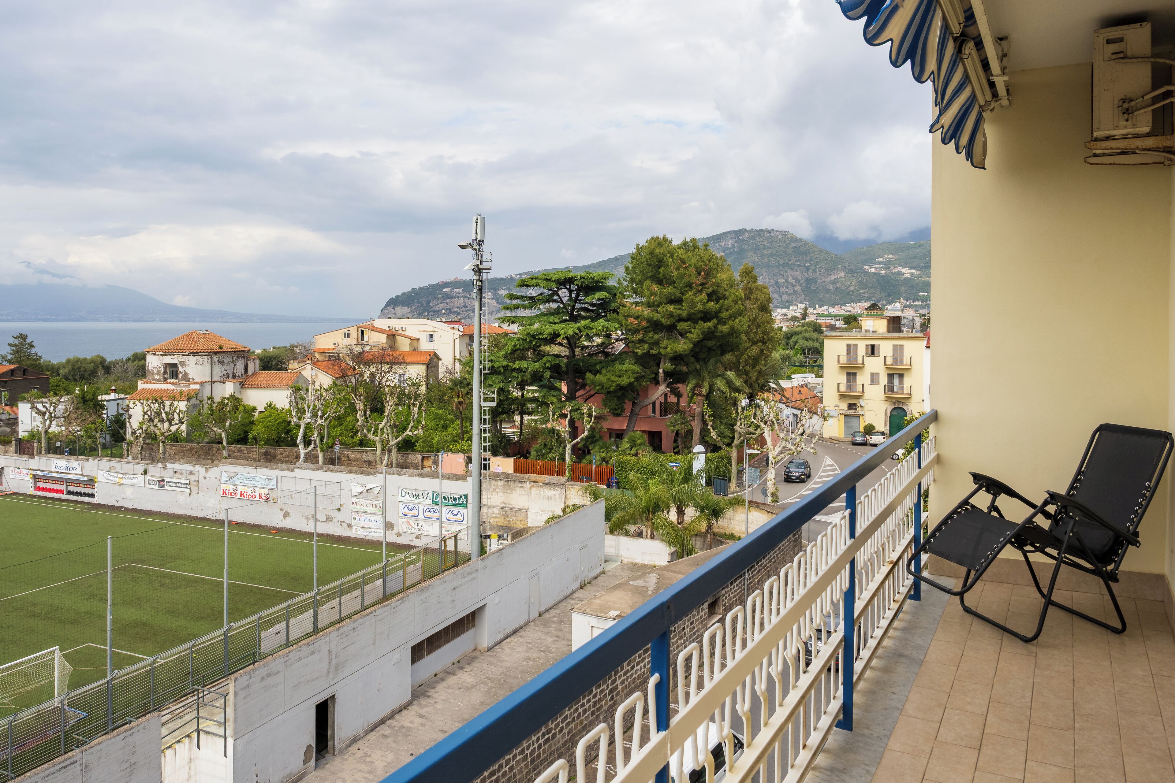 A balcony with a view of a sports field, buildings, and a mountain in the distance.