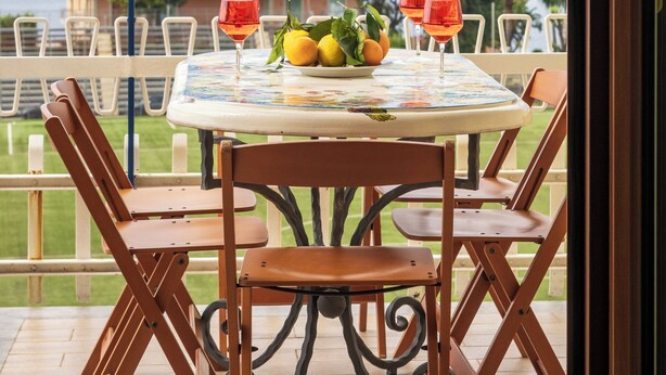 A table with a fruit bowl and two glasses of red wine, set on a balcony overlooking a body of water and buildings. - Residenza Le Sirene (Sorrento)