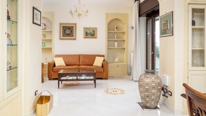 A living room with a brown sofa, a glass coffee table, a large vase, and a chandelier. - Residenza Le Sirene (Sorrento)