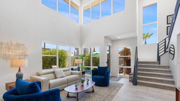 A spacious living area with a high ceiling, large windows, a staircase, and a view of the outdoors. - Designer Palm Springs Retreat | Private Spool · Mtn Views · 3BR · Pets Welcome (Palm Springs)