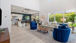 A spacious living area with a sofa, chairs, a coffee table, and a kitchen in the background. - Designer Palm Springs Retreat | Private Spool · Mtn Views · 3BR · Pets Welcome (Palm Springs)