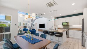 A modern kitchen with white cabinets, a stainless steel refrigerator, and a flat-screen TV. - Designer Palm Springs Retreat | Private Spool · Mtn Views · 3BR · Pets Welcome (Palm Springs)