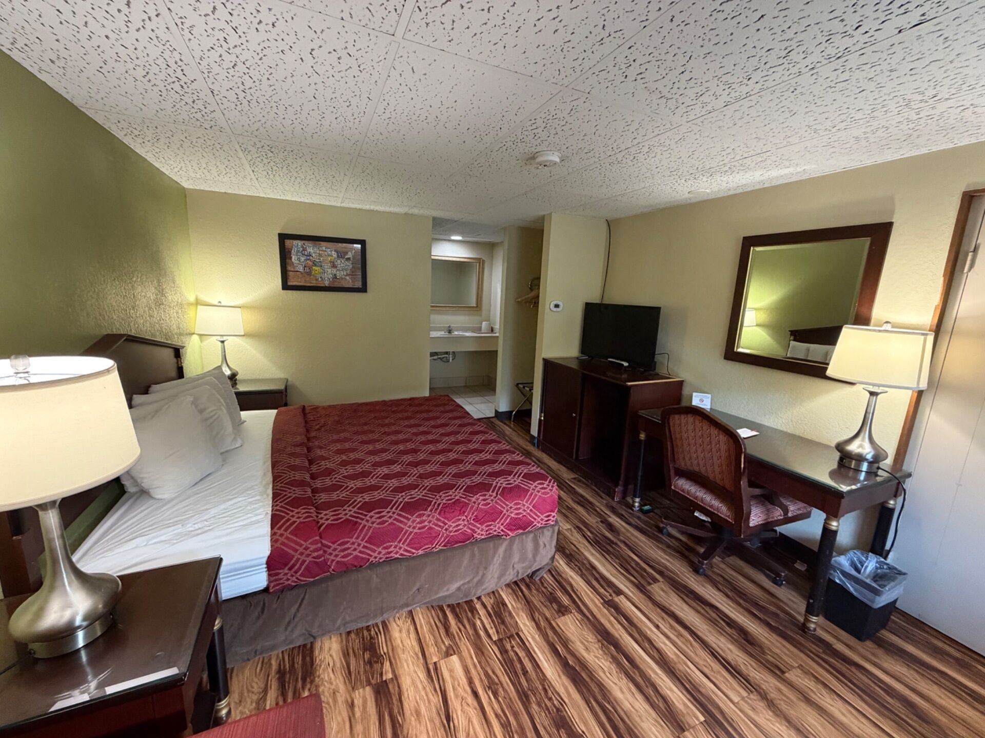 A hotel room with a bed, desk, chair, television, and a bathroom visible in the background.