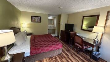 A hotel room with a bed, desk, chair, television, and a bathroom visible in the background.