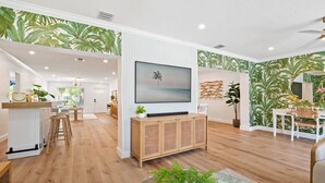 Ein modernes Wohnzimmer mit Flachbildfernseher, Holzboden und tropischem Wandpapier.