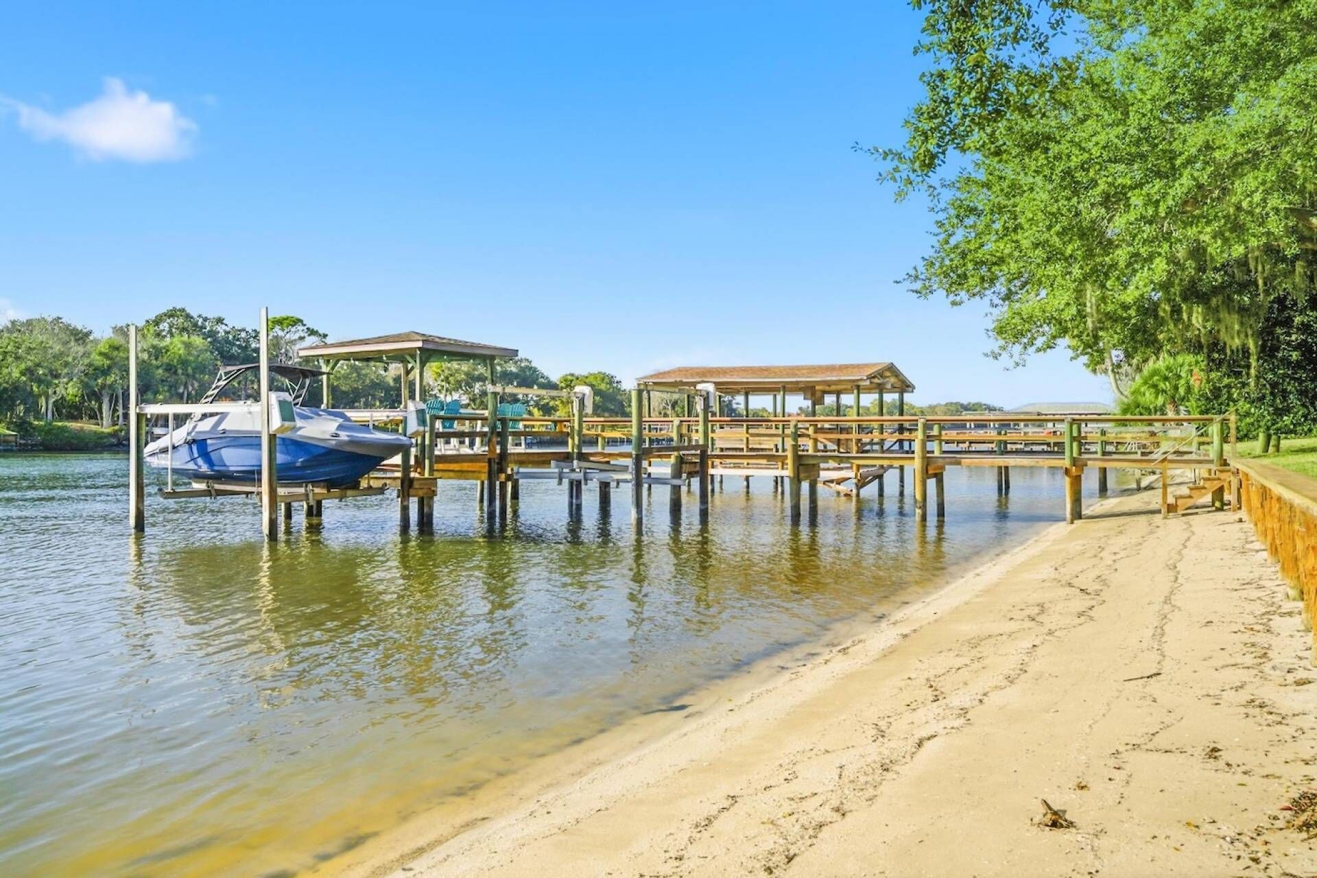 Ein Strand mit einer Holzsteganlage, ein Boot, das an der Anlegestelle liegt, und einem überdachten Sitzbereich.