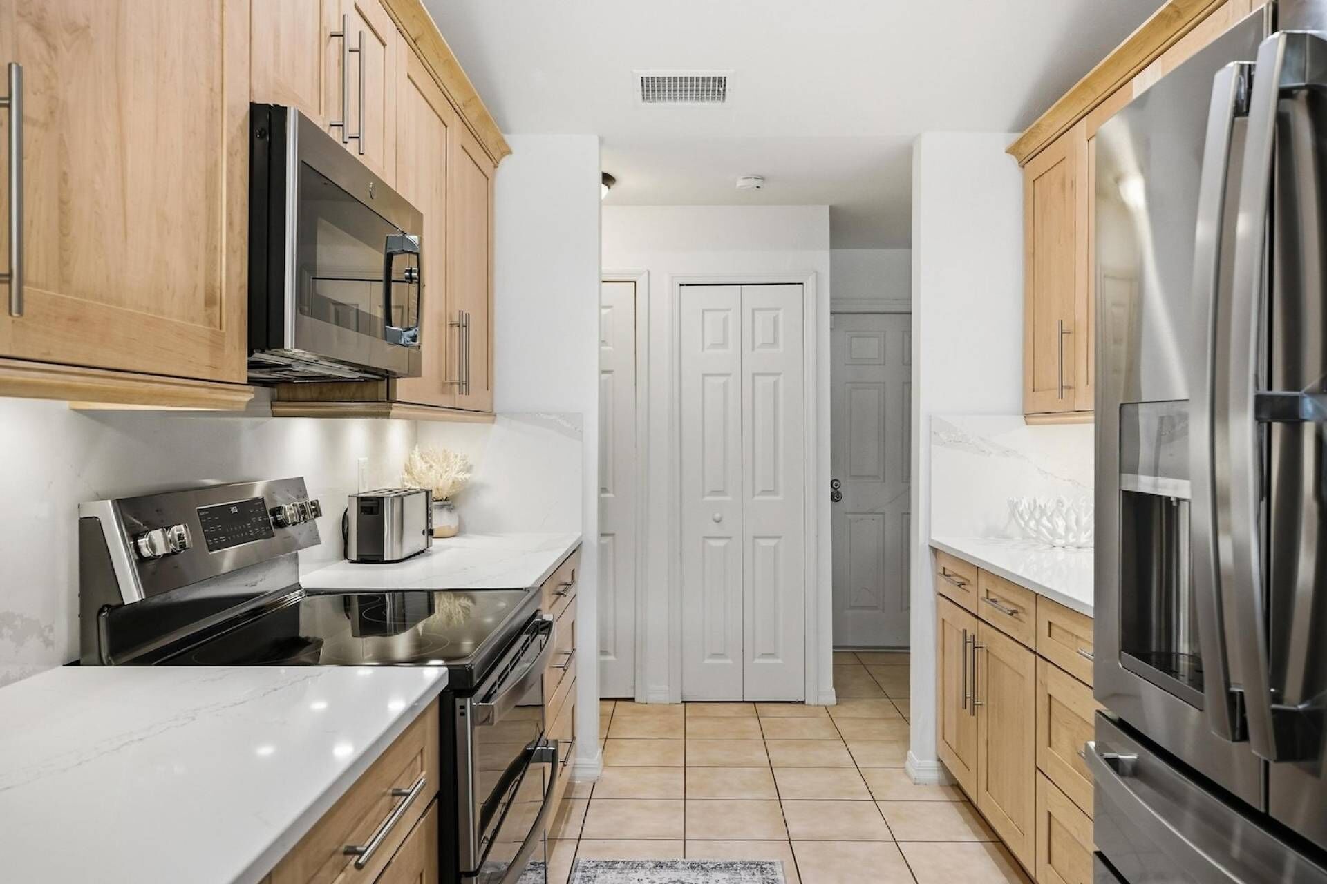 A modern kitchen with wooden cabinets, stainless steel appliances, and a white door in the center.