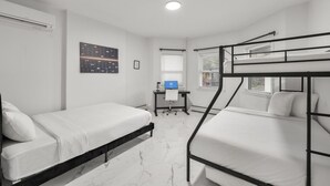 Een slaapzaal met stapelbedden, een bureau met een computer, een raam en een luchtverkoeler aan de muur.
