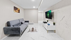 Een moderne woonkamer met een grijze bank, een wandtelevisie en een marmeren vloer.