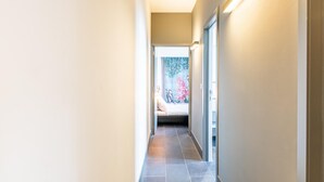 Un couloir étroit, avec une porte au fond qui donne sur une pièce où se trouve un lit.
