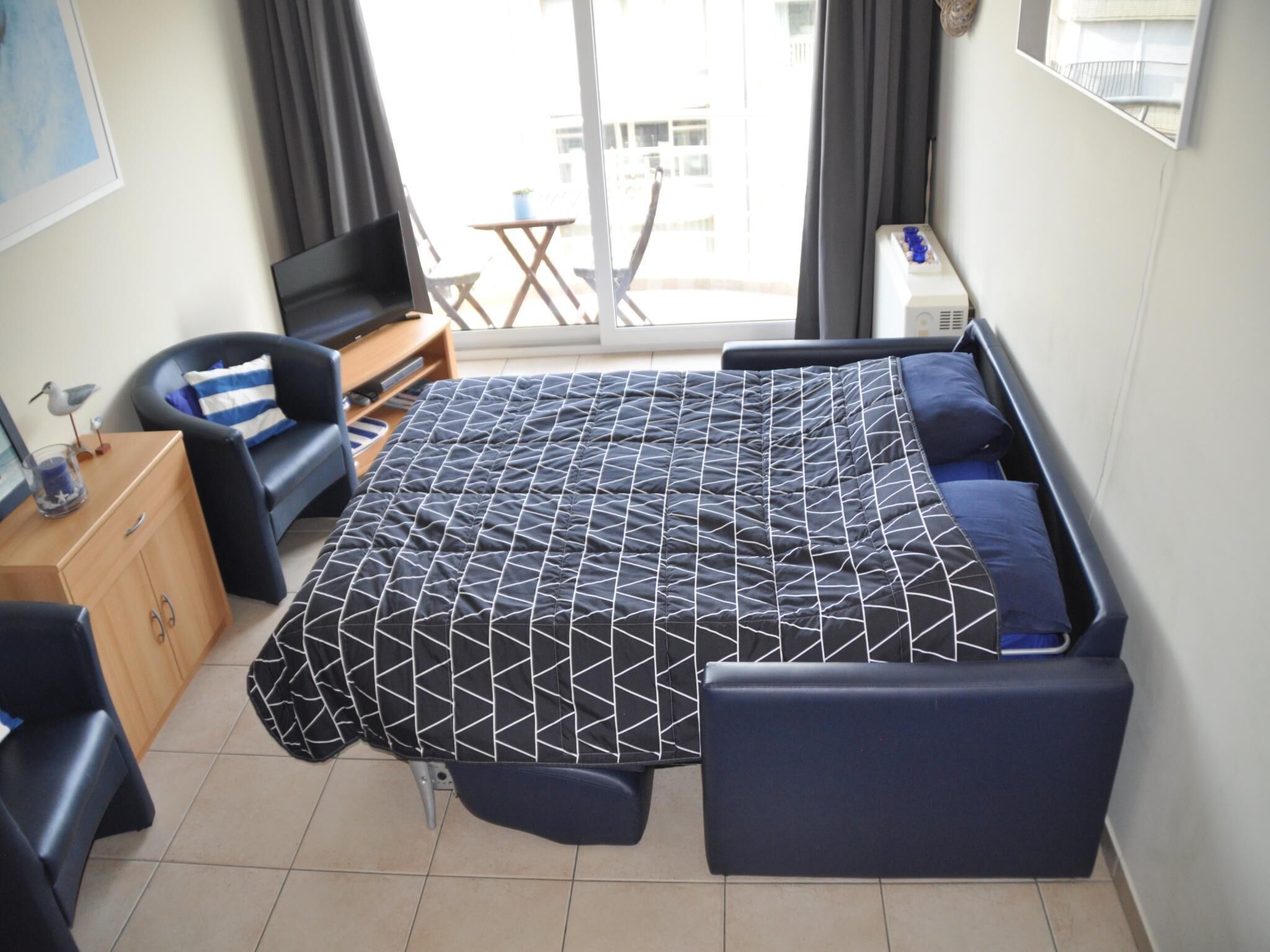 Ein modernes Zimmer mit einem Bett, einem Schreibtisch, einem Sessel und einem Fernseher.