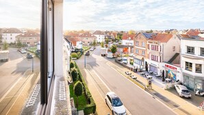 Vista de la calle desde una ventana con vistas a una zona residencial con casas, tiendas y cielo despejado.