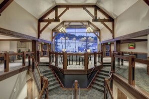 Un intérieur spacieux avec un escalier central, des poutres en bois et une vue sur un paysage enneigé grâce à de grandes fenêtres.