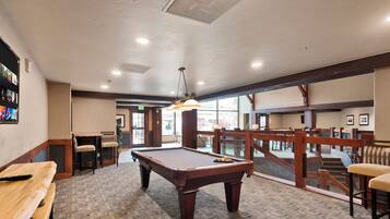 Une table de billard dans une pièce dotée de bancs en bois, d’un luminaire suspendu et offrant une vue à travers de grandes fenêtres.