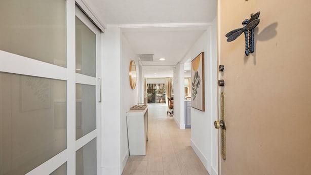 A hallway with a sliding glass door, a door with a decorative dragonfly, and a view into a living area with a sofa and a coffee table. - Gorgeous Iconic Villa Alejo Condo, One Block from Downtown (Palm Springs)