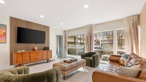 A modern living room with a flat-screen TV, wooden cabinet, leather sofas, and a large sliding glass door leading to a balcony. - Gorgeous Iconic Villa Alejo Condo, One Block from Downtown (Palm Springs)