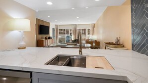 A modern kitchen with a built-in sink, a dining area with a table and chairs, and a living room with a sofa and TV. - Gorgeous Iconic Villa Alejo Condo, One Block from Downtown (Palm Springs)
