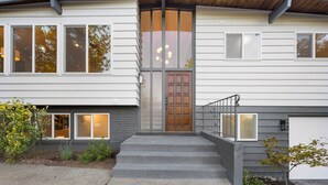 Une maison moderne à deux étages, dotée d’une porte d’entrée en bois, de grandes fenêtres et d’un escalier en béton menant à l’entrée.