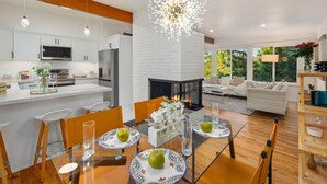Une cuisine moderne avec des meubles blancs, un îlot central et un coin repas doté d’une table en verre pour quatre personnes.