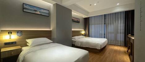 A hotel room with two beds, a nightstand, a desk, and a large window with curtains.