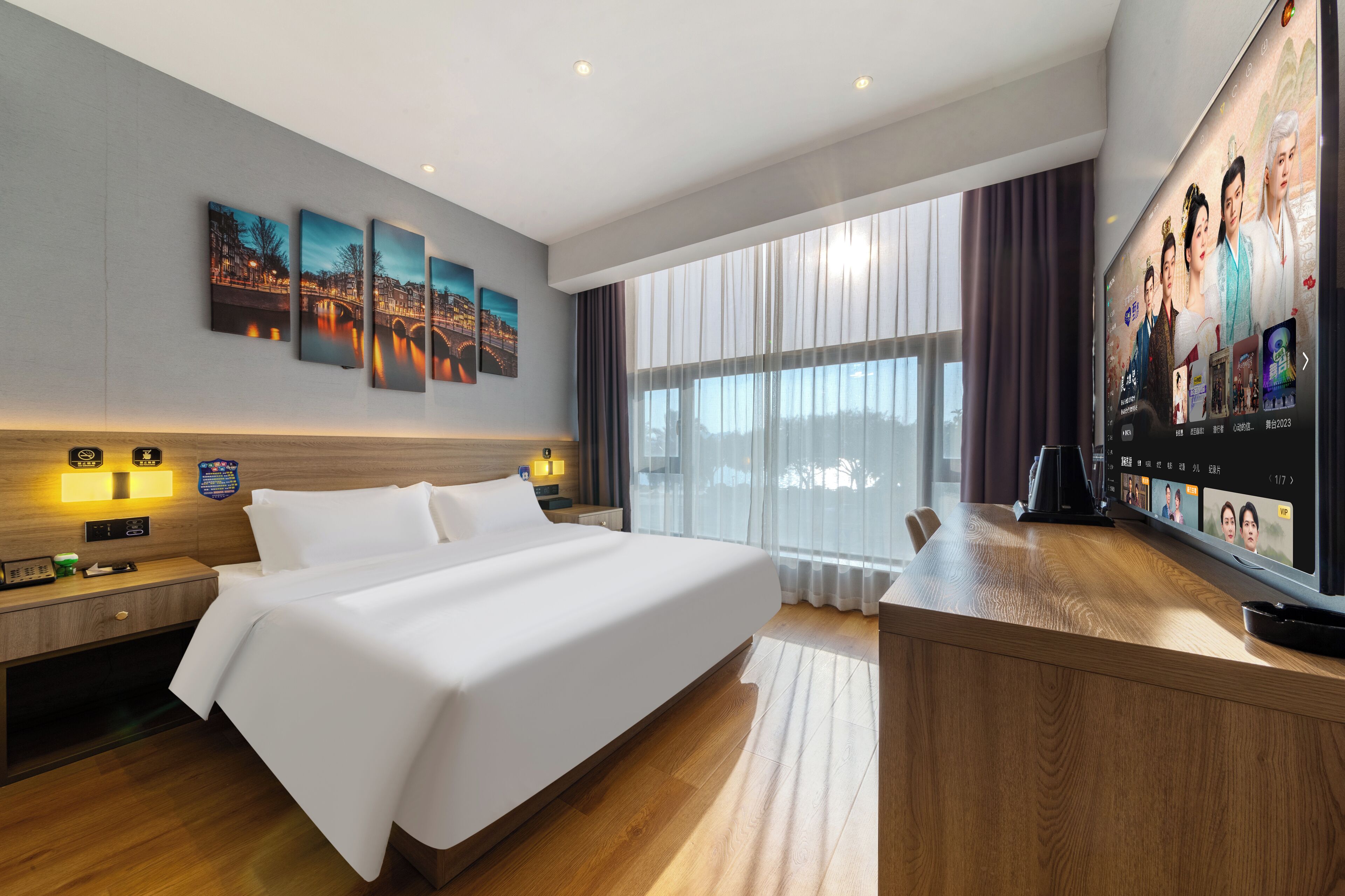 A modern hotel room with a large bed, a TV, and artwork on the wall.