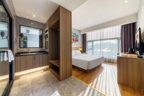 A modern hotel room with a large bed, a wooden desk, a bathroom with a mirror and sink, and a large window with curtains. - ZHONG SHAN HAI BIN (Xiamen)