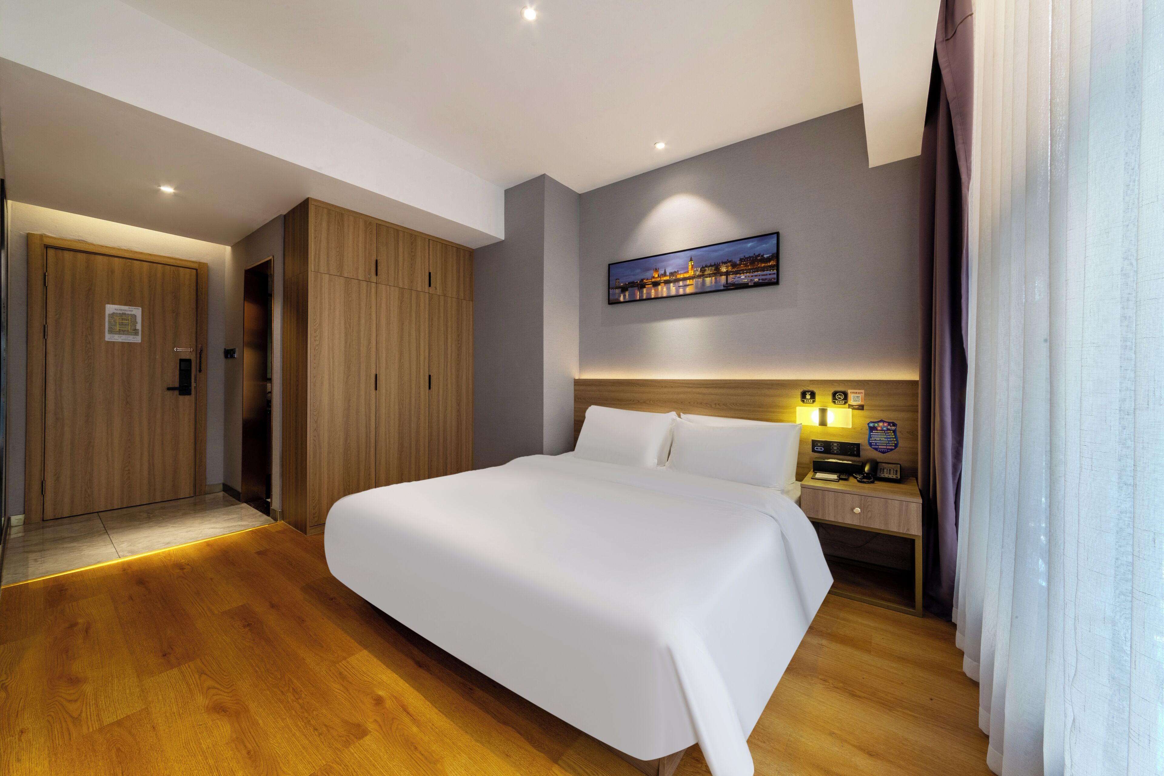 Une chambre d’hôtel moderne avec un grand lit, une armoire en bois et une table de chevet avec une lampe.