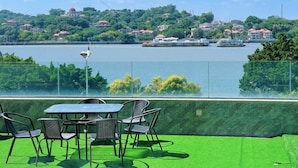 Une terrasse avec une table et des chaises, donnant sur une rivière où l’on aperçoit des bateaux et des maisons au loin.