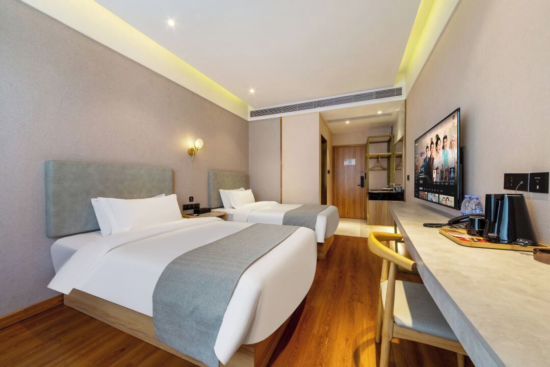 Habitación de hotel con dos camas, un escritorio, un televisor y un espejo.
