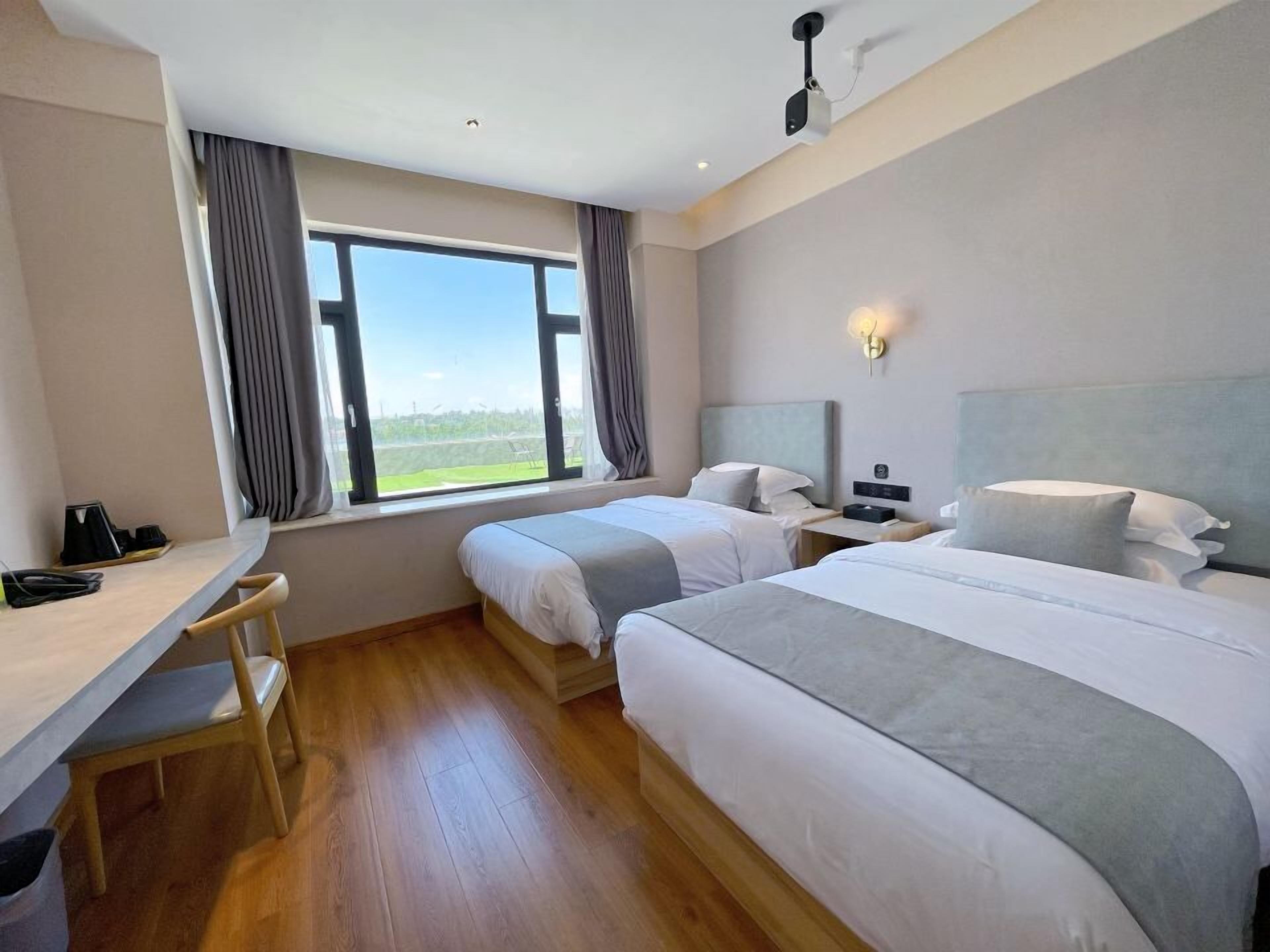 Habitación de hotel con dos camas, un escritorio, una silla, una mesita de noche y una ventana con cortinas.