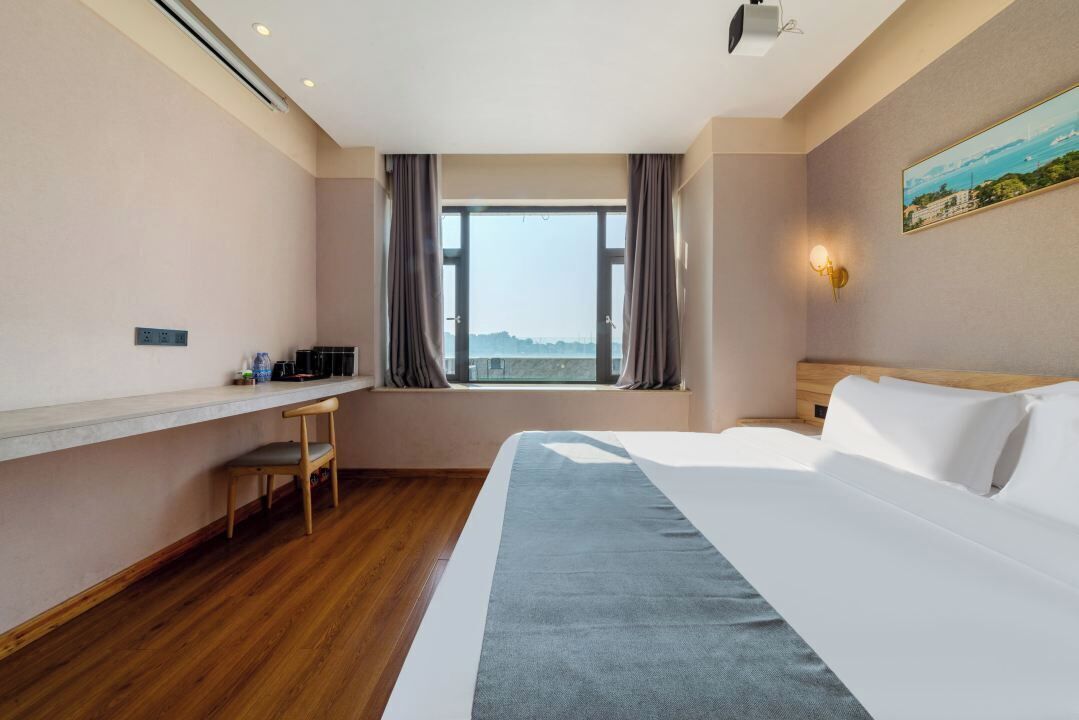 Ein Hotelzimmer mit Bett, Schreibtisch, Stuhl, einem Fenster mit Aussicht und einem Bild an der Wand.