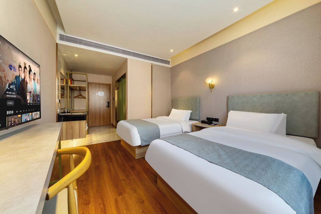 A hotel room with two beds, a desk, a TV, and a bathroom visible through an open door.