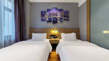 A hotel room with two beds, a cityscape artwork on the wall, a nightstand with a phone and lamp, and a window with curtains.