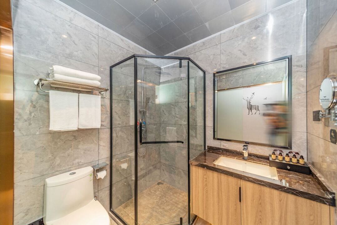Une salle de bain moderne avec une douche à parois de verre, des toilettes, un lavabo doté d'un plan de travail en marbre et un grand miroir.