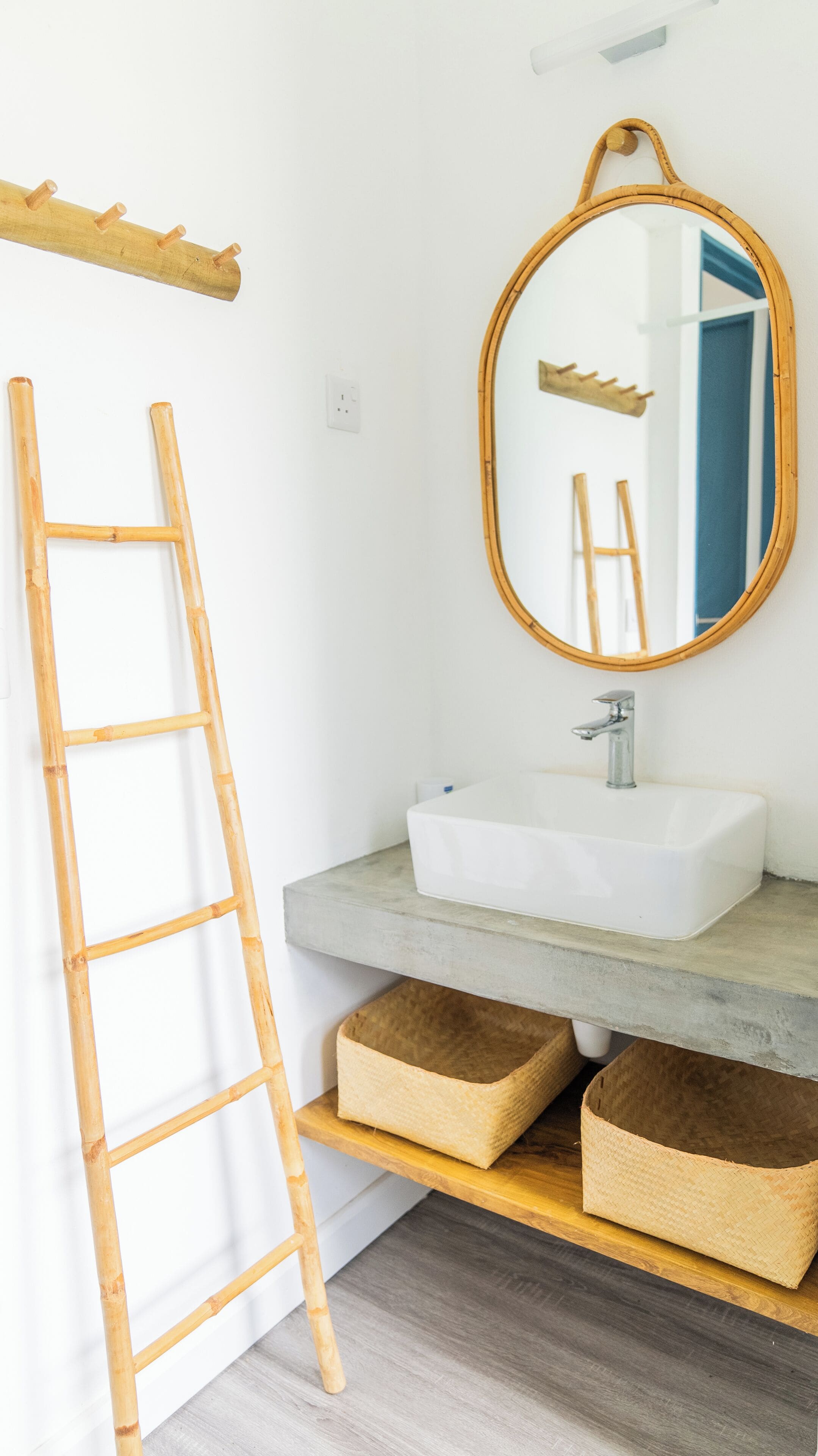 A bathroom with a wooden ladder, a round mirror, a white sink, and two woven baskets on a shelf.