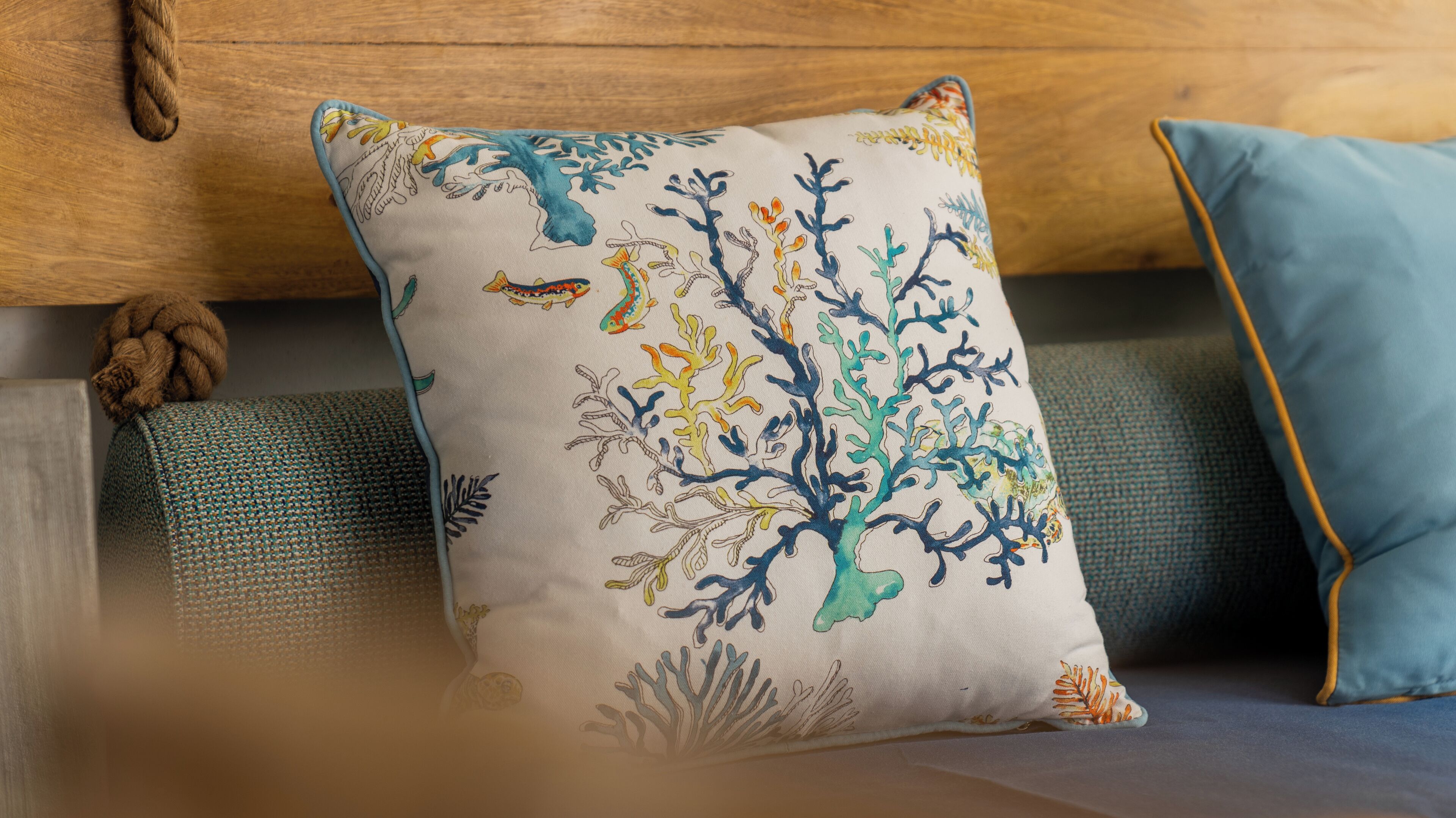 A cushion with a coral reef design, placed on a textured sofa.