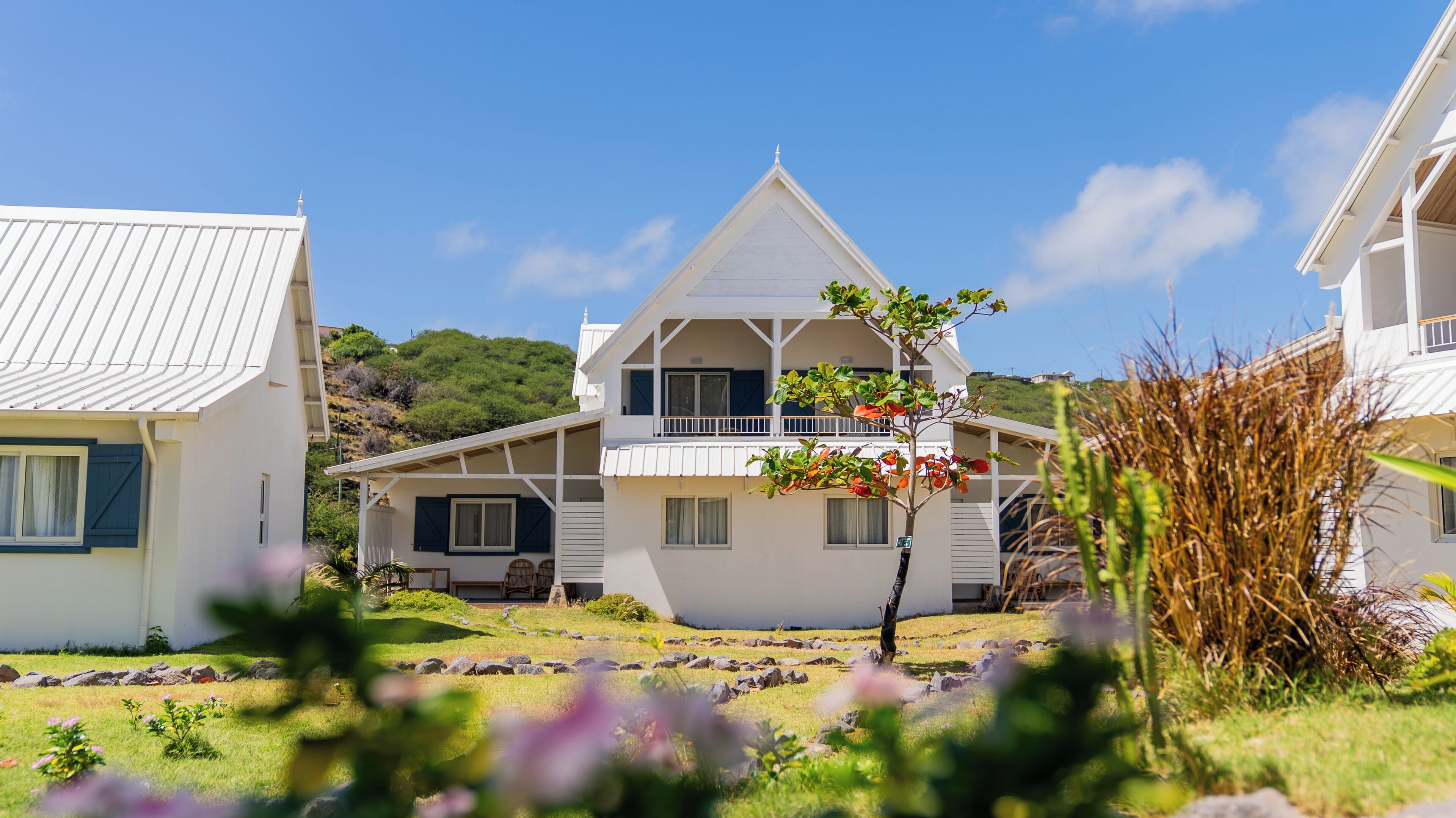 A two-story house with a balcony, surrounded by a garden with rocks and plants.
