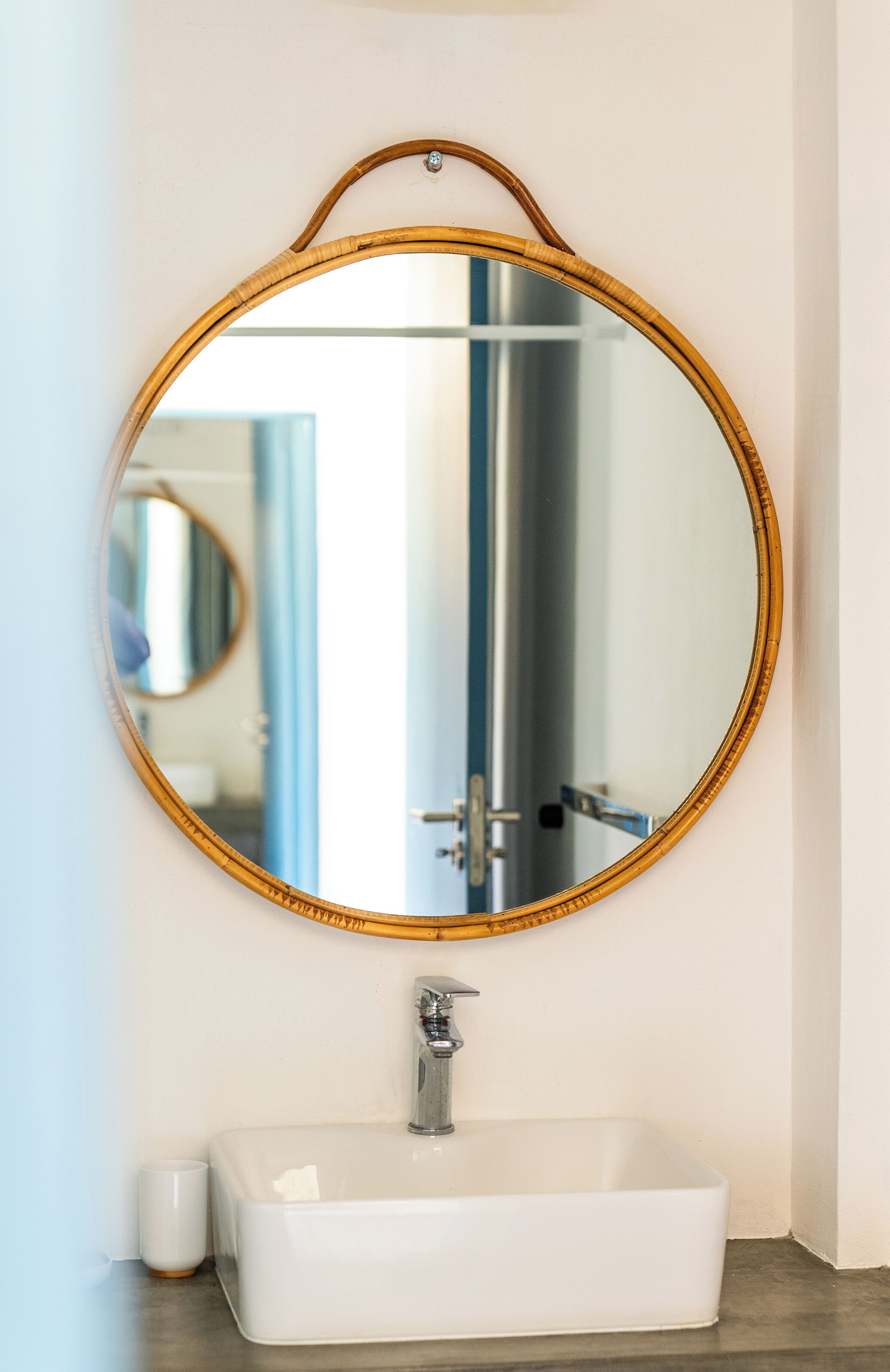 A bathroom with a round mirror, a rectangular sink, and a small white cup on the counter.