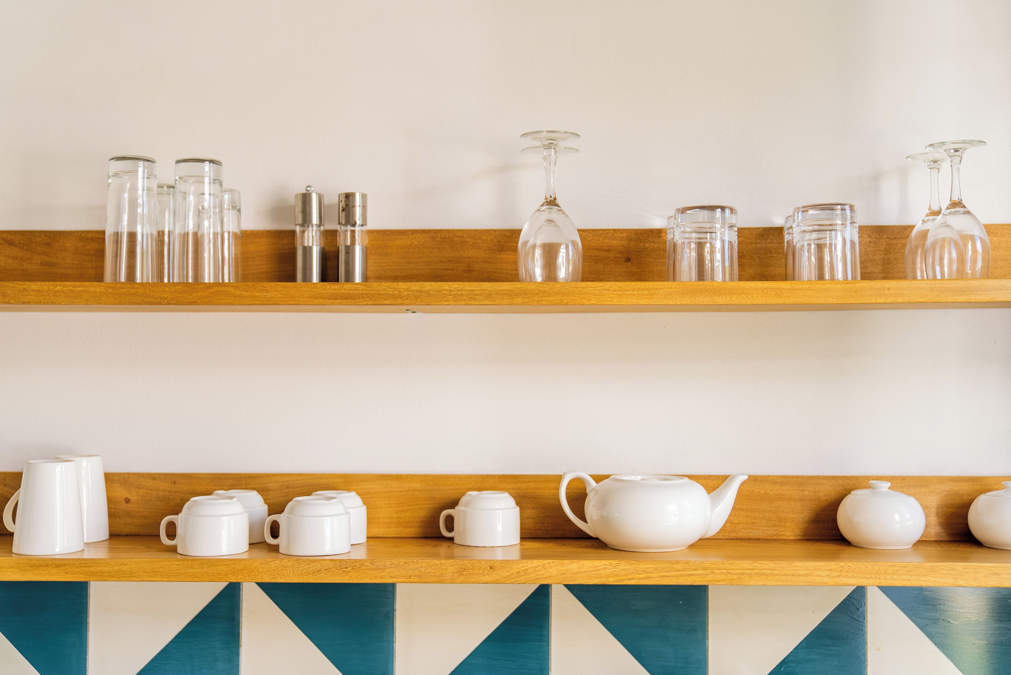 Two wooden shelves with white ceramic tea sets and glassware.