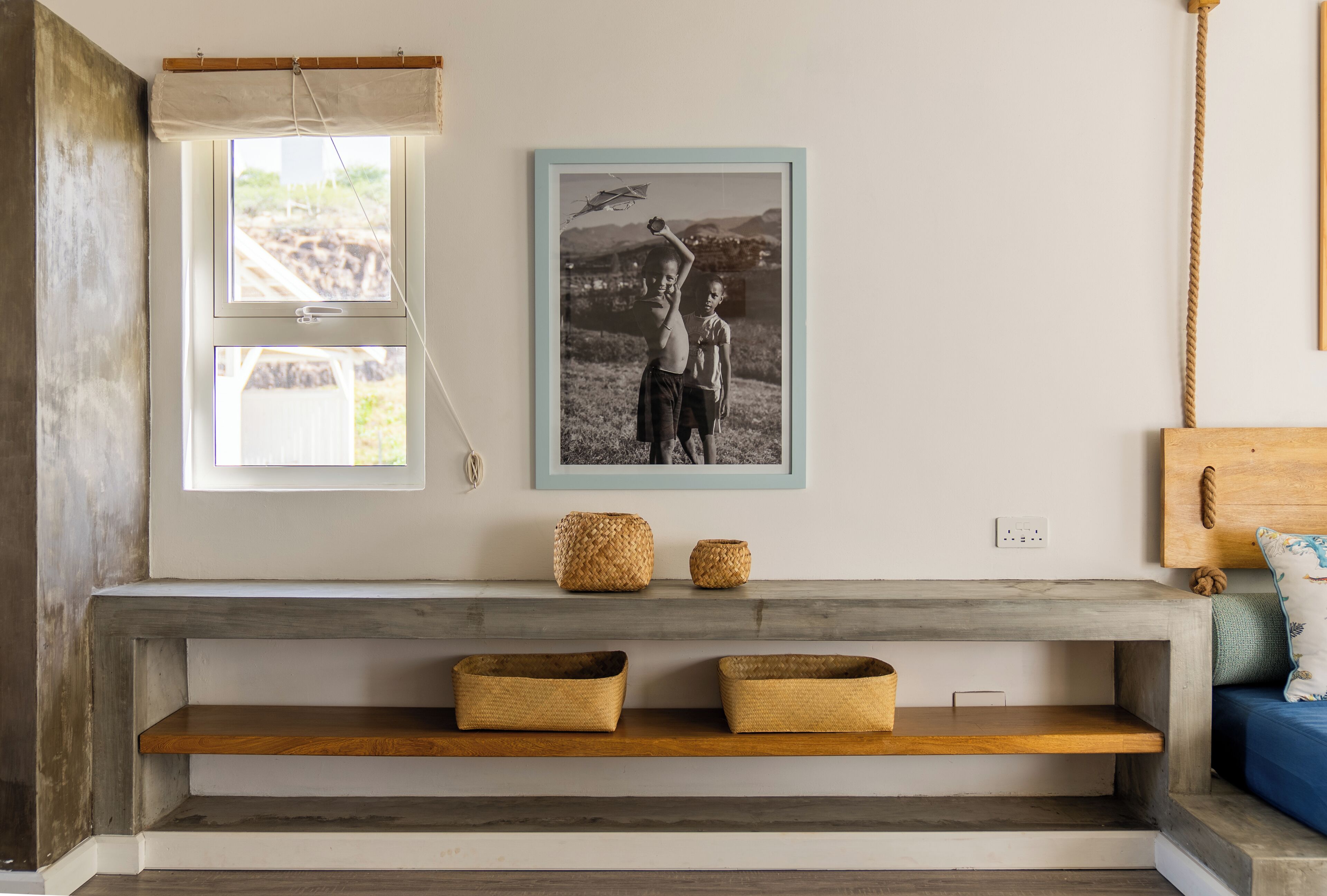 A room with a bench, two baskets, a framed photo, and a window with a curtain.