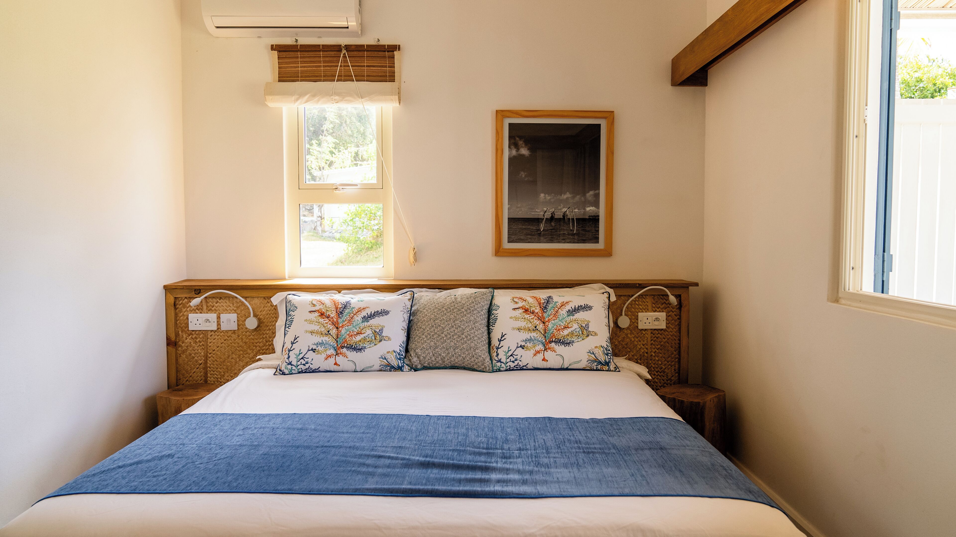 Un dormitorio con cama, dos ventanas, aire acondicionado de pared y un cuadro enmarcado.