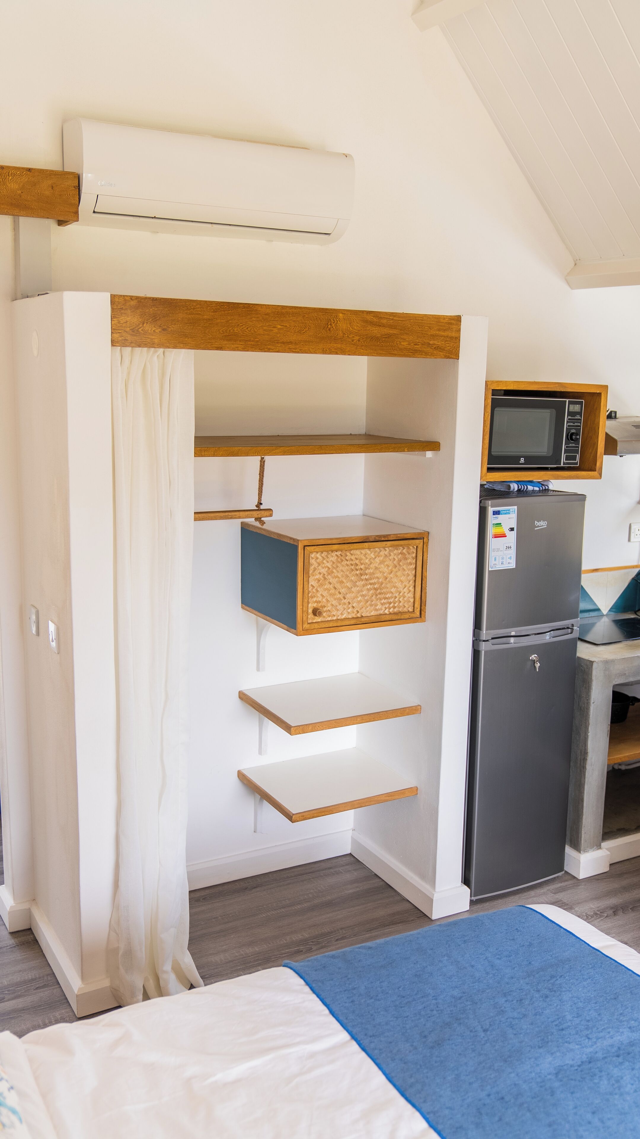 Une petite cuisine équipée comprenant un micro-ondes encastré, un réfrigérateur et des étagères en bois.