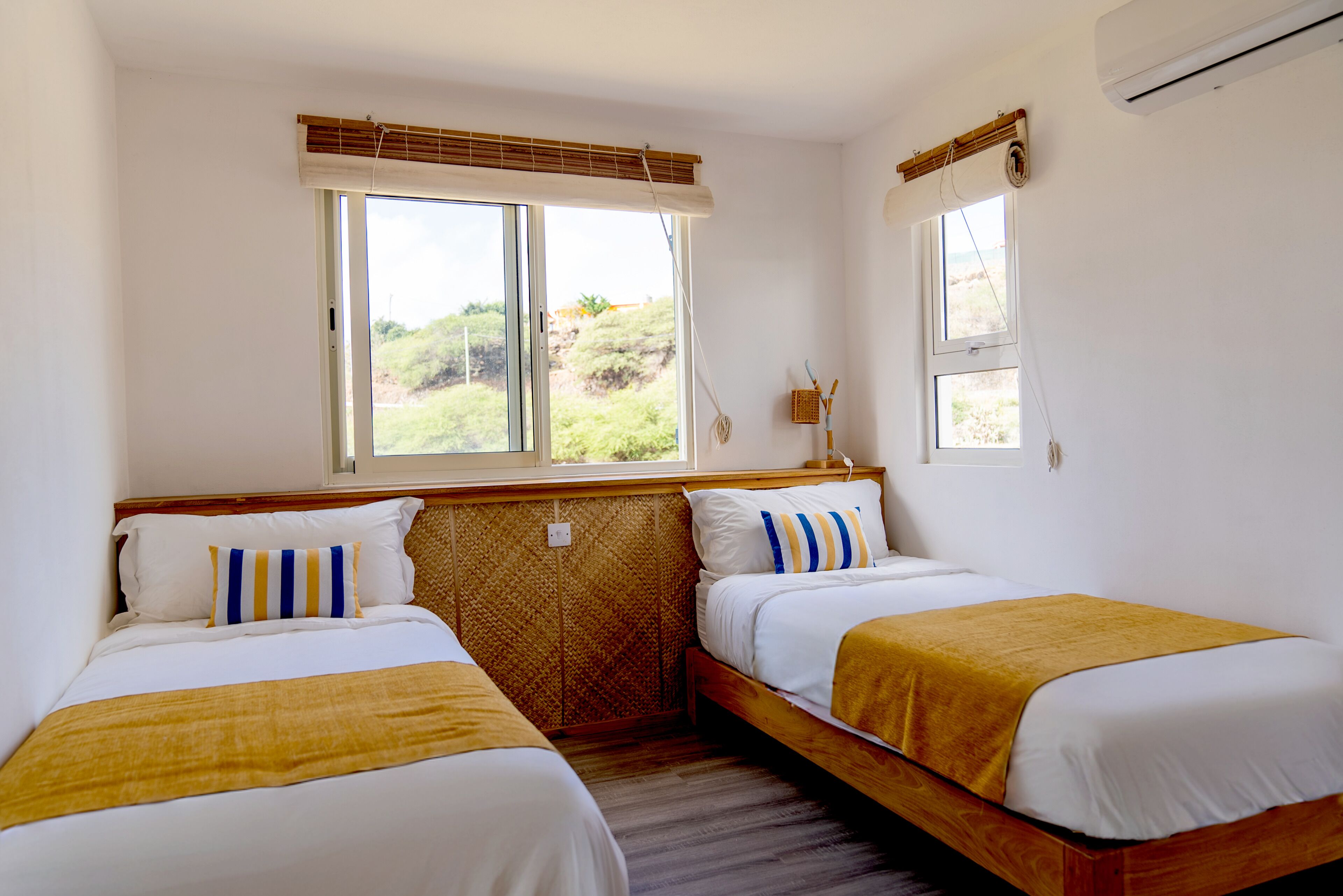 Une chambre avec deux lits, une fenêtre donnant sur un espace verdoyant et un climatiseur fixé au mur.