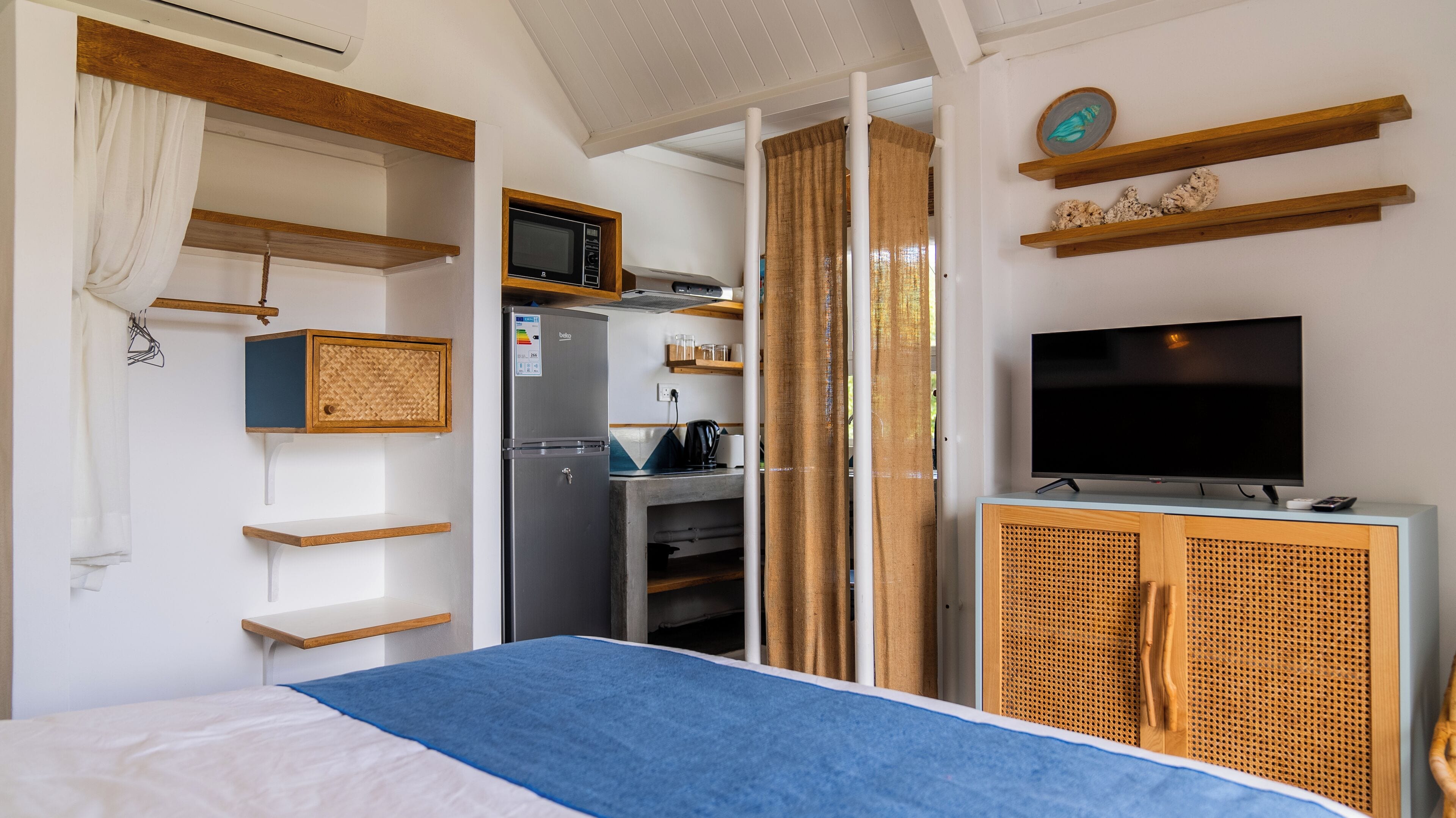 Une chambre d’hôtel équipée d’un lit, d’une télévision, d’une kitchenette et d’une salle de bain, le tout visible à travers une porte coulissante.