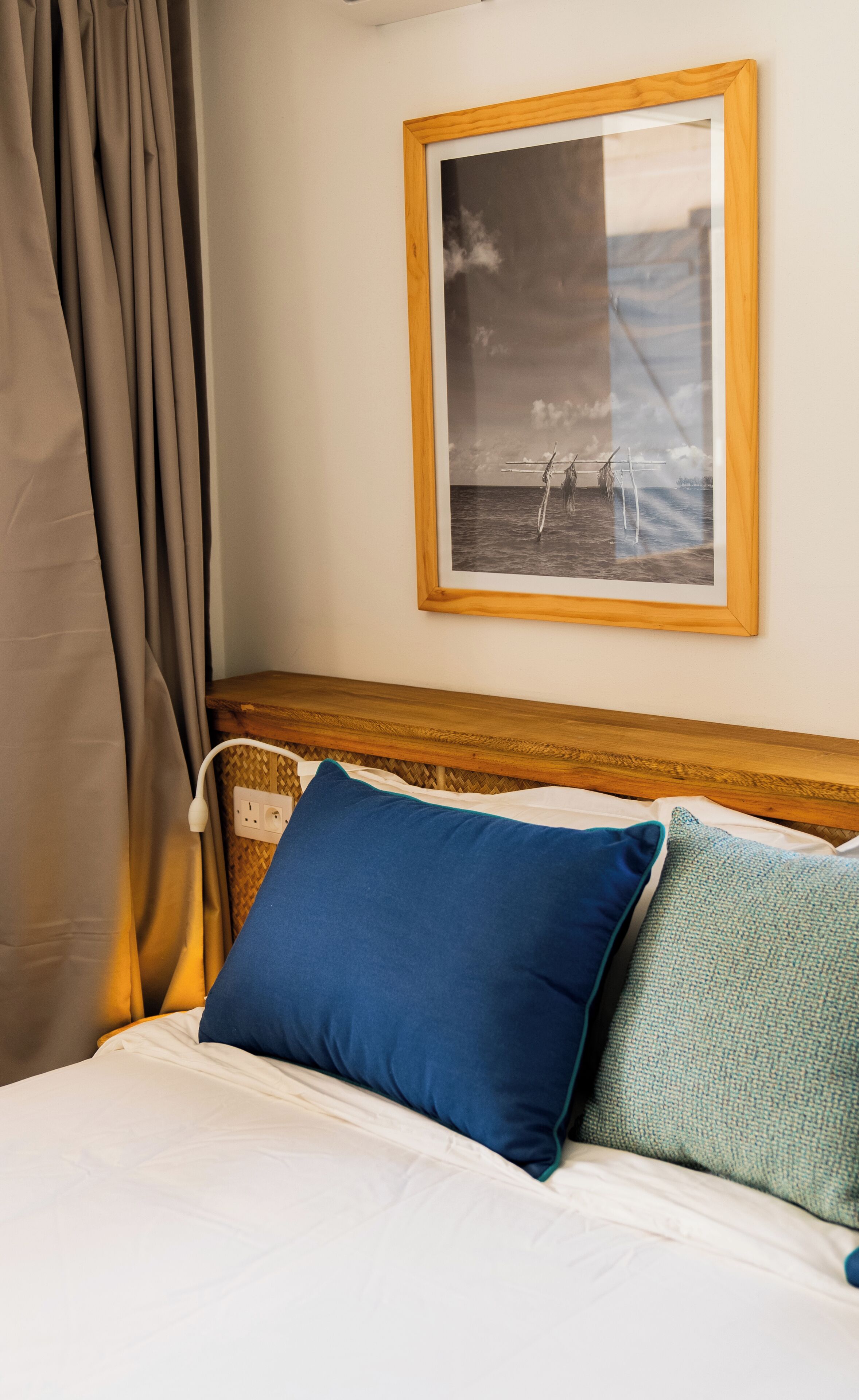 A neatly made bed with white bedding and two pillows, one blue and one green, in a room with a wooden headboard and a framed picture on the wall.