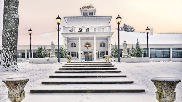 Un imposant bâtiment à la façade symétrique, doté de grandes fenêtres et d’une entrée centrale, laquelle est encadrée par des marches menant à l’intérieur.