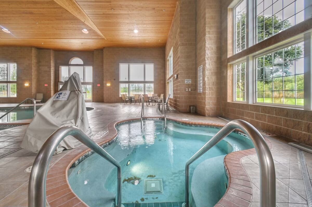 Una piscina interior con agua cristalina, rodeada de paredes de ladrillo y grandes ventanales.