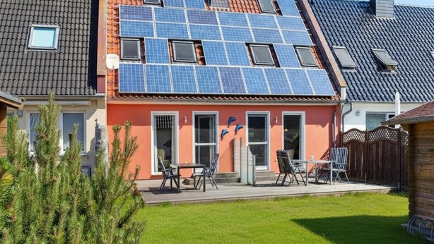 Een woonhuis met een schuin dak, zonnepanelen en een klein terras met tuinmeubilair.